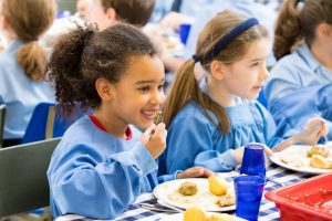 Pupils eating cooked lunch together in dining hall